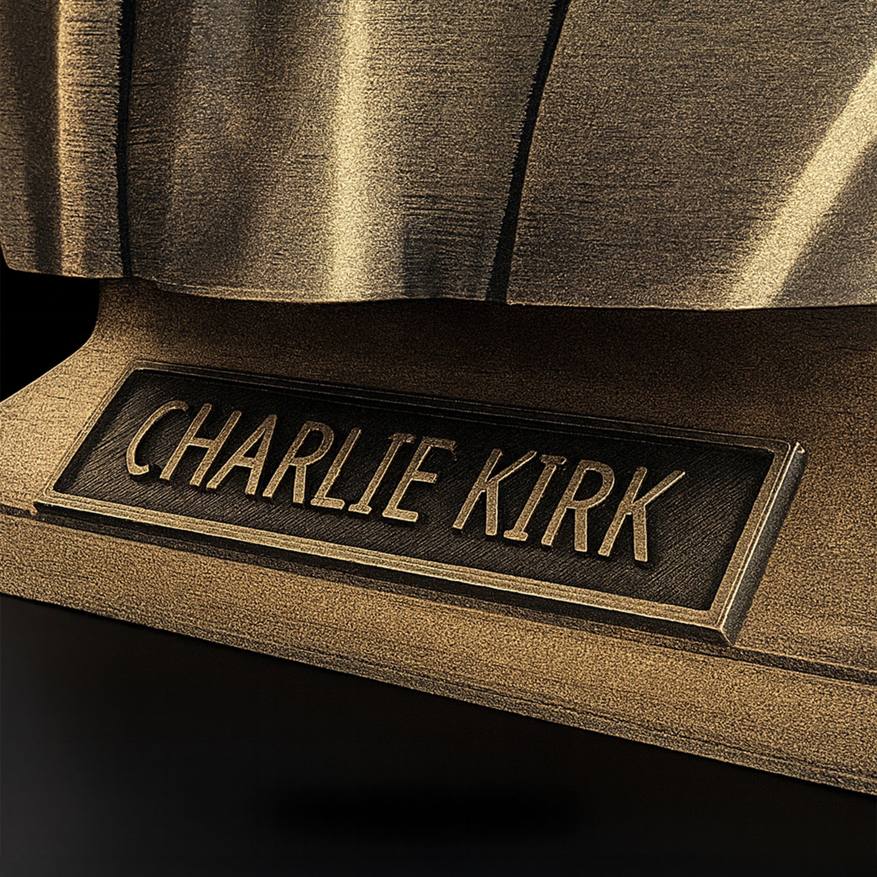 Charlie Kirk bust gold nameplate close-up — engraved plaque reflective finish